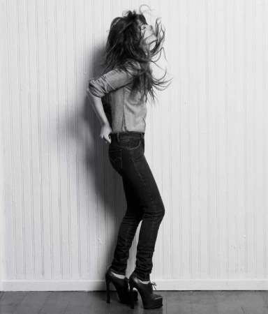 Woman in dark jeans and button-down shirt tossing her hair back against vertical wood paneling, photographed by Lauren Dukoff.