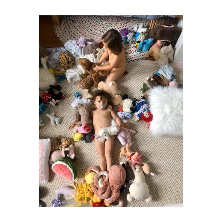 Overhead shot of two young children surrounded by stuffed animals on a patterned rug, creating a playful and whimsical scene.