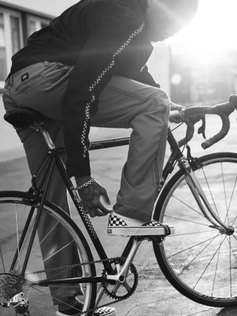 A person riding a bicycle, showcasing Vans checkered shoes and clothing with matching pattern, in a black and white photograph.