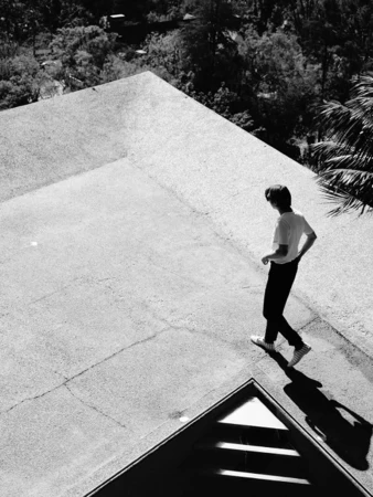 High-angle black and white photograph of a person walking on a rooftop next to dense trees.