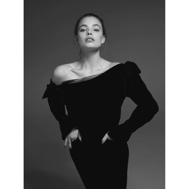 Striking black-and-white studio portrait of a woman in a black velvet dress, hands on hips, looking directly at the camera with neutral expression.