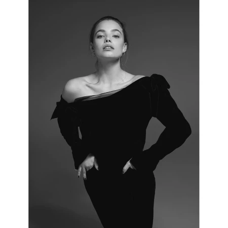 Striking black-and-white studio portrait of a woman in a black velvet dress, hands on hips, looking directly at the camera with neutral expression.