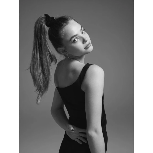 Monochrome portrait of a woman in a black dress. She is turned to the side but looking back at the camera over her shoulder.