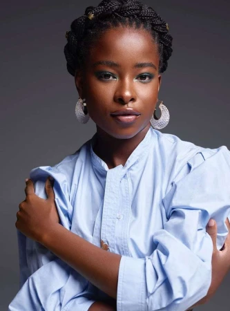 Portrait of a black woman wearing a light blue button-down shirt and statement hoop earrings against a dark grey background.
