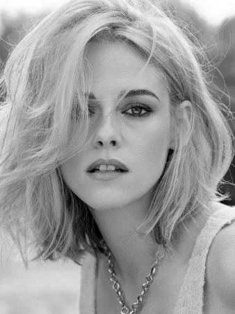 Close-up portrait of Kristen Stewart in black and white wearing a textured sleeveless top and a chunky chain necklace.