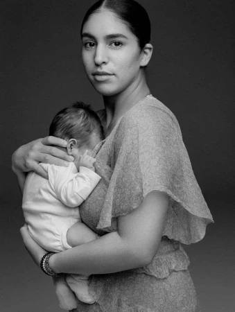 Monochrome portrait of a woman holding an infant against a dark studio background