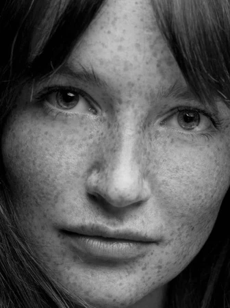 Close-up monochrome portrait of a woman with heavy freckles and bangs, photographed by Lauren Dukoff.
