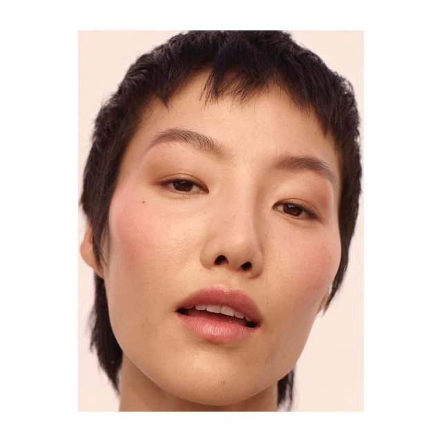 Close-up beauty shot of an Asian woman with short dark hair, light skin, and soft, pink makeup against a neutral background.