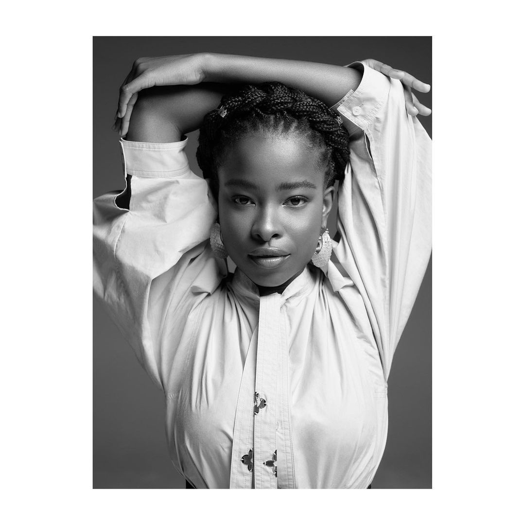 Black and white portrait of a young Black woman with braided hair, wearing an oversized collared shirt against a gradient background.