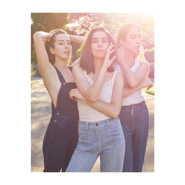 Three women posing in a sunlit outdoor setting. They are wearing casual denim and tops, with soft lighting highlighting their features.