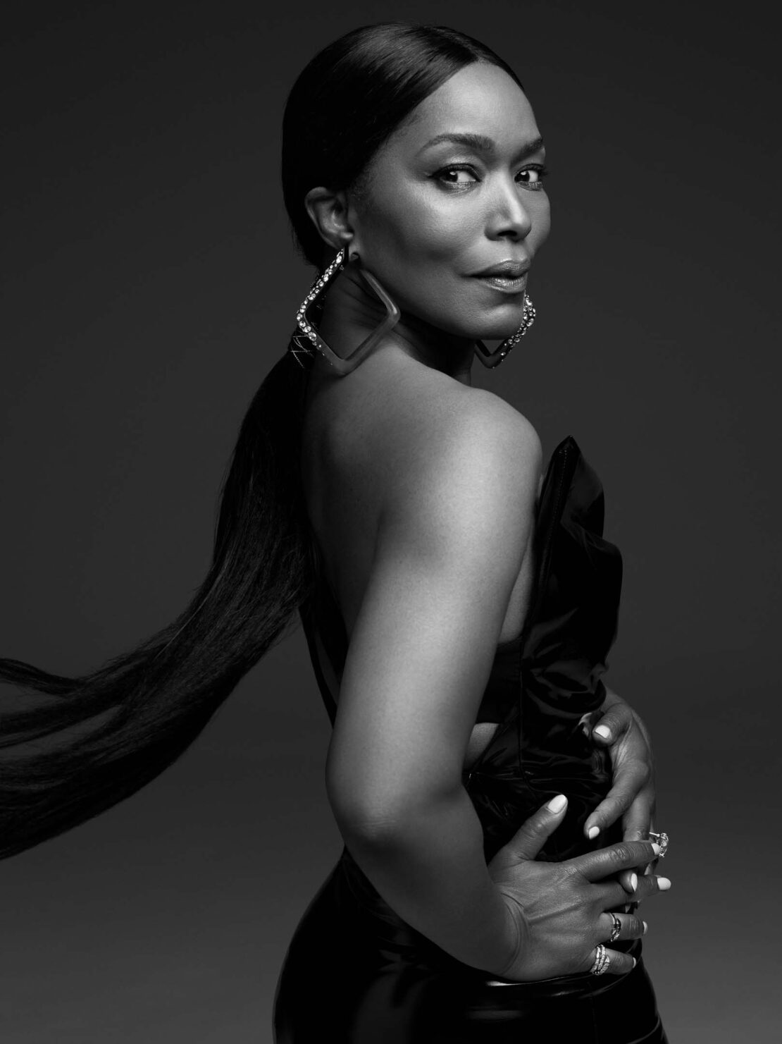 Black and white portrait of a Black woman in a black dress and large earrings, looking over her shoulder in a studio setting.