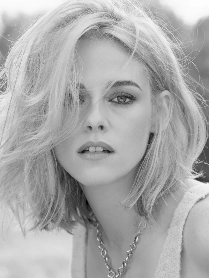 Black and white portrait of actress Kristen Stewart with blonde hair and dark eye makeup wearing a chain necklace