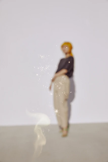 Woman with red hair and a dark top poses in front of a white wall with sparklers. Out of focus with shallow depth of field.