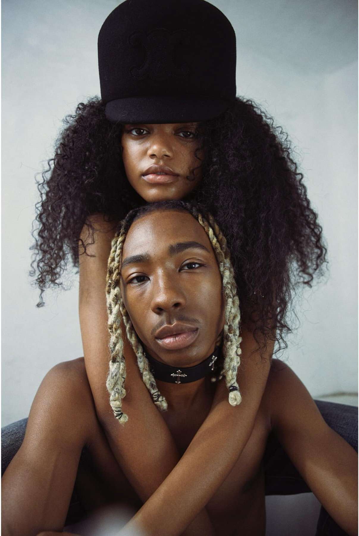 Close-up fashion portrait of a young adult African American woman in a black hat embracing a young adult Black man with blonde braids.