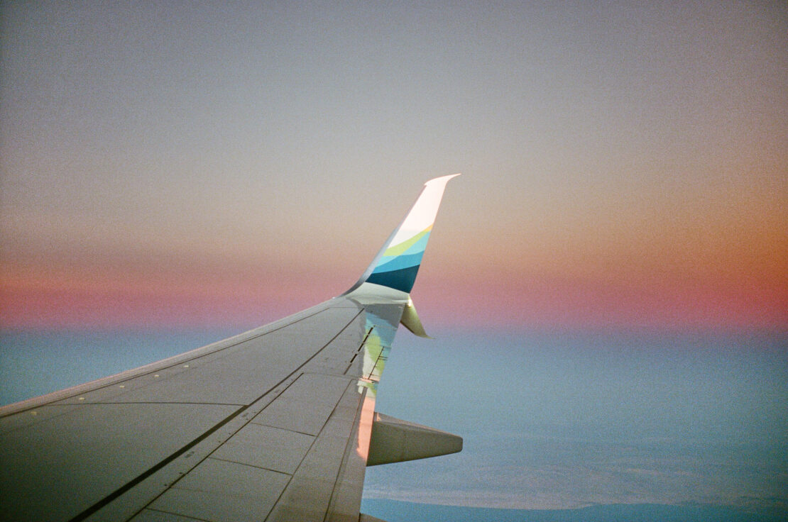 Airplane wing during flight with the sky and horizon visible in the background, shot from inside the aircraft, travel concept, aerial view.