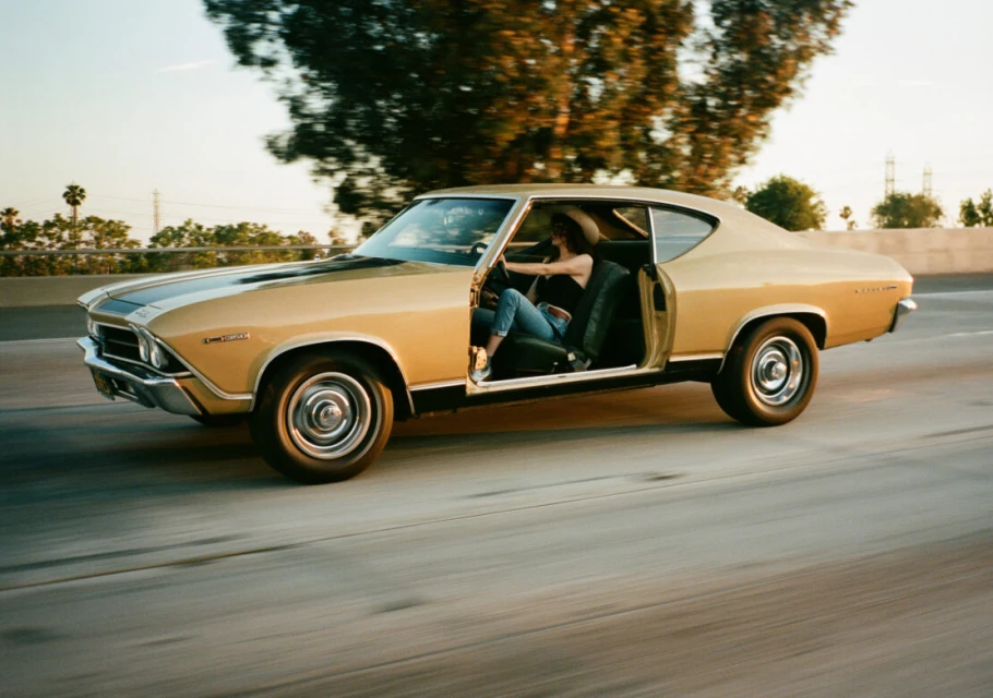 Woman driving a vintage gold muscle car on a highway during golden hour, showcasing classic automotive design and open-road adventure.