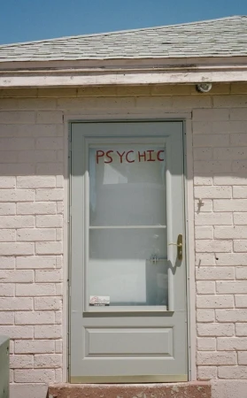 Exterior shot of a white brick building featuring a pale grey door with frosted glass that reads 'Psychic' in red lettering.