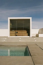 Modern architectural sauna with glass walls and wooden interior overlooking a concrete swimming pool under a blue sky.