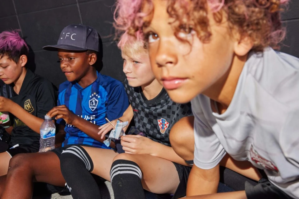 Group of young soccer players in team jerseys sitting, resting, and eating snacks after a game with dyed pink hair. Close angle.