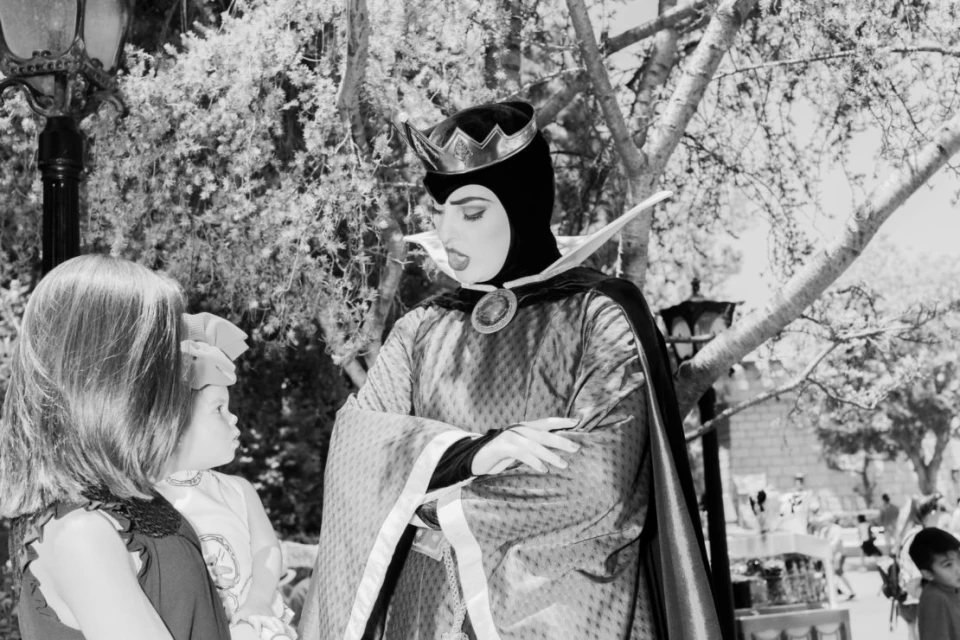 A person cosplaying as the Evil Queen stands outdoors with an audience, wearing a crown and black and purple robe with a tall collar.