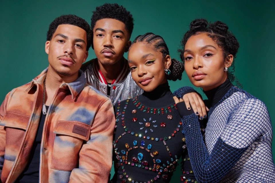 Four young adults pose against a green backdrop. Two women with styled hair and natural makeup flank two young men in fashionable jackets.