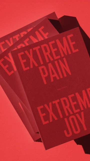 Stack of red book covers featuring text 'EXTREME PAIN' and 'EXTREME JOY' on a matching solid red background, creating a visually striking contrast.