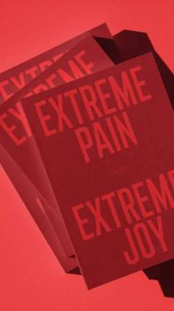 Stack of red book covers featuring text 'EXTREME PAIN' and 'EXTREME JOY' on a matching solid red background, creating a visually striking contrast.