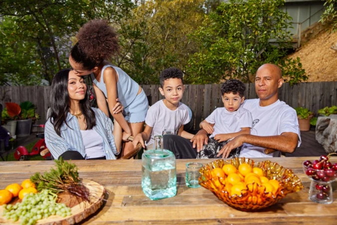 Family seated around a wooden outdoor table loaded with fruit, captured by photographer Maggie Shannon.