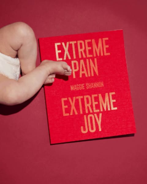 Baby's leg and foot rest on a bright red book titled 'Extreme Pain Extreme Joy' by Maggie Shannon, creating a compelling visual.
