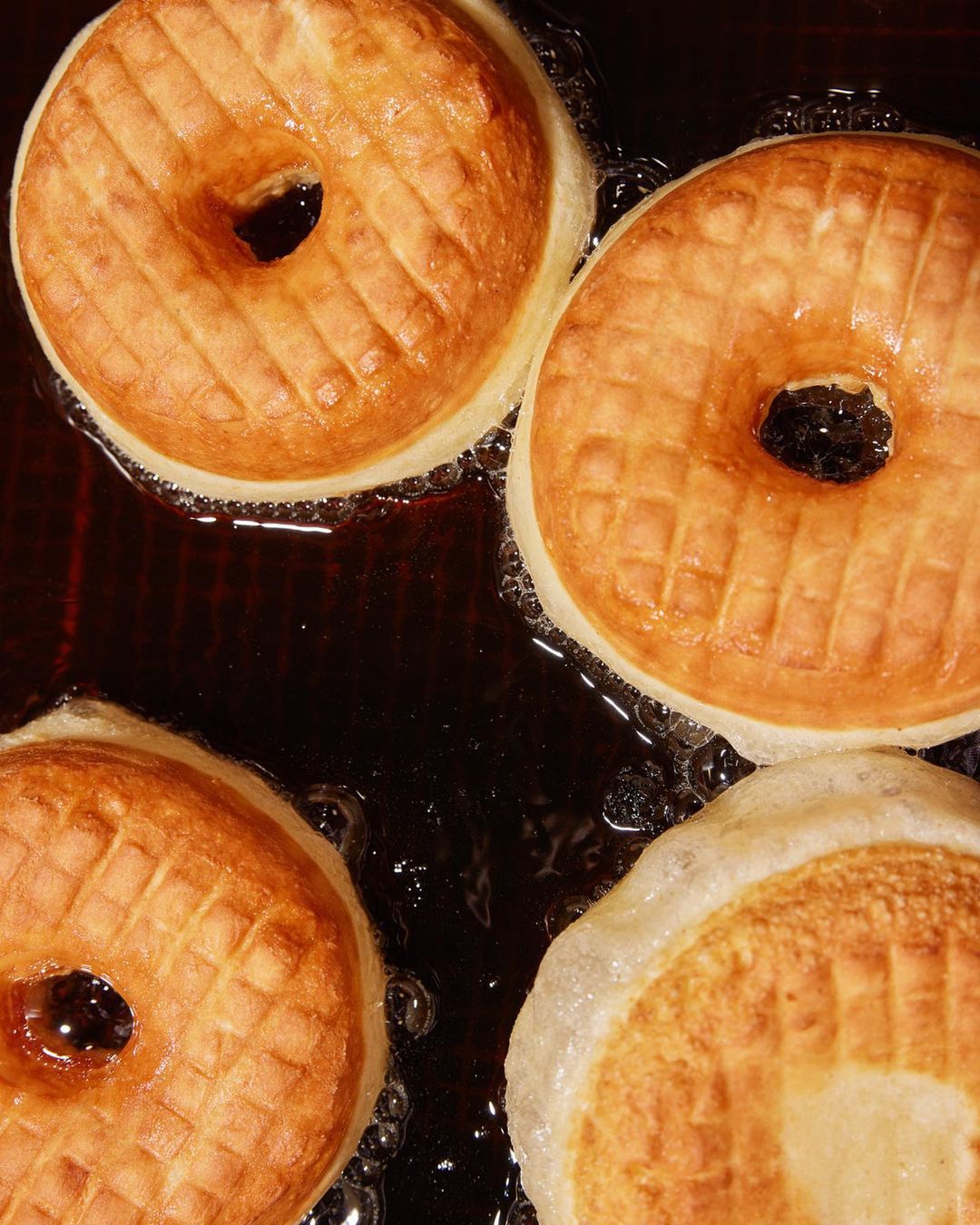 Golden-brown donuts frying in hot oil, showcasing their textured surface and bubbly surroundings. Close-up food photography.