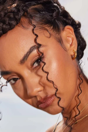 Close-up portrait of a woman with braided hair and tight ringlet tendrils, wearing small gold hoop earrings.