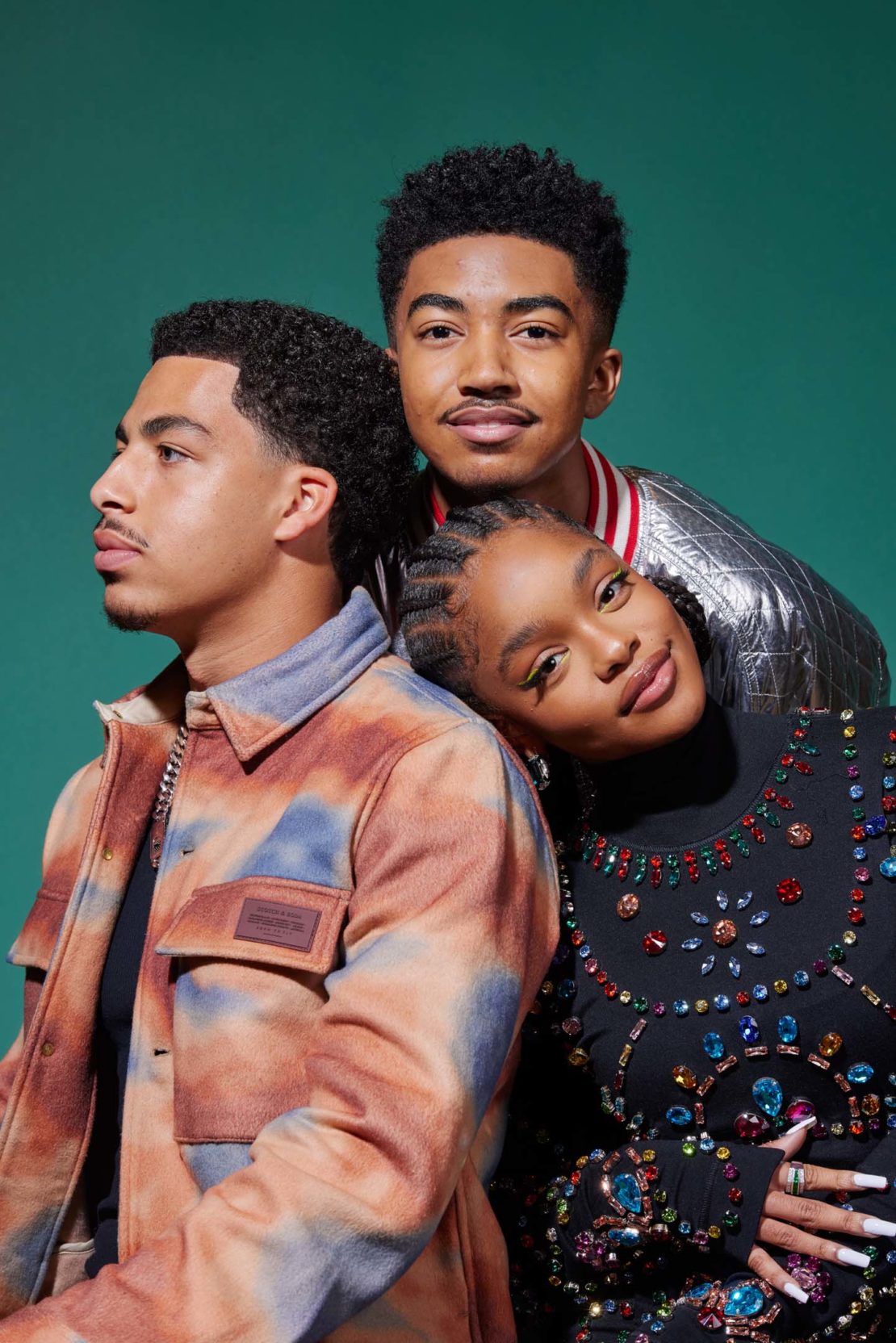 A group studio portrait features three young adults looking stylish against a green backdrop, capturing a modern and fashionable aesthetic.