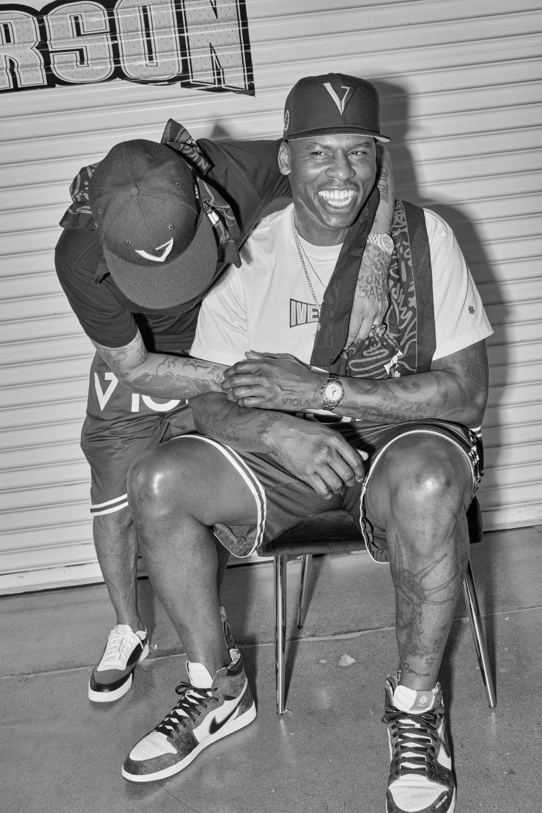 Black and white portrait of two adult men in casualwear posing indoors with a garage door in the background, showcasing urban style and friendship.