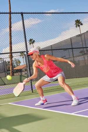 Woman playing pickleball on outdoor court. Active woman in sportswear swings paddle at yellow ball in a clear sky setting.