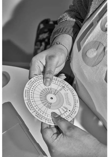 Person holding a PetroGard disc calculator to determine the days in each month in a black and white studio image, close up.