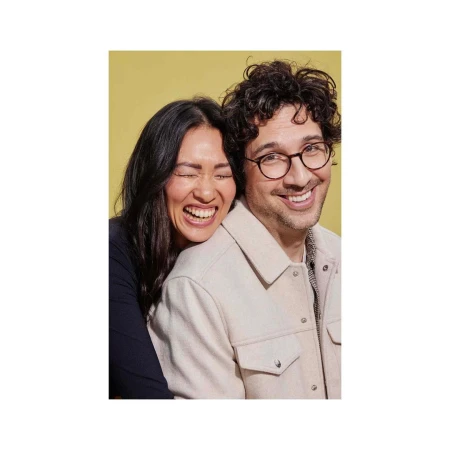 A smiling couple with the woman hugging the man, posing in a studio setting with a yellow background, capturing a joyful and intimate moment.