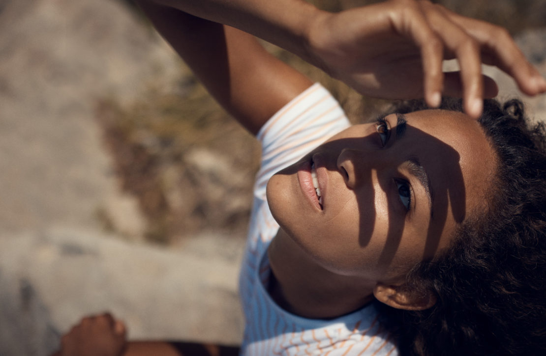 Close-up of a young woman looking up with her hand shading her face, casting strong hand shadows across her features.