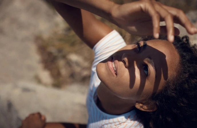 Close-up of a young woman looking up with her hand shading her face, casting strong hand shadows across her features.