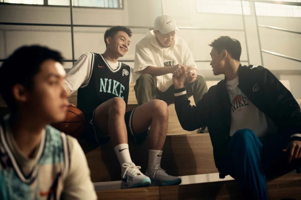 Four young men wearing sports and casual clothing are sitting on stairs in an indoor environment, all wearing Nike-branded attire.