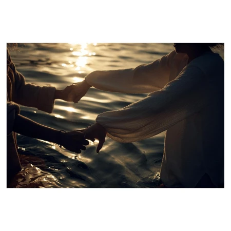 Two people holding hands while standing waist-deep in water at sunset, captured in silhouette.