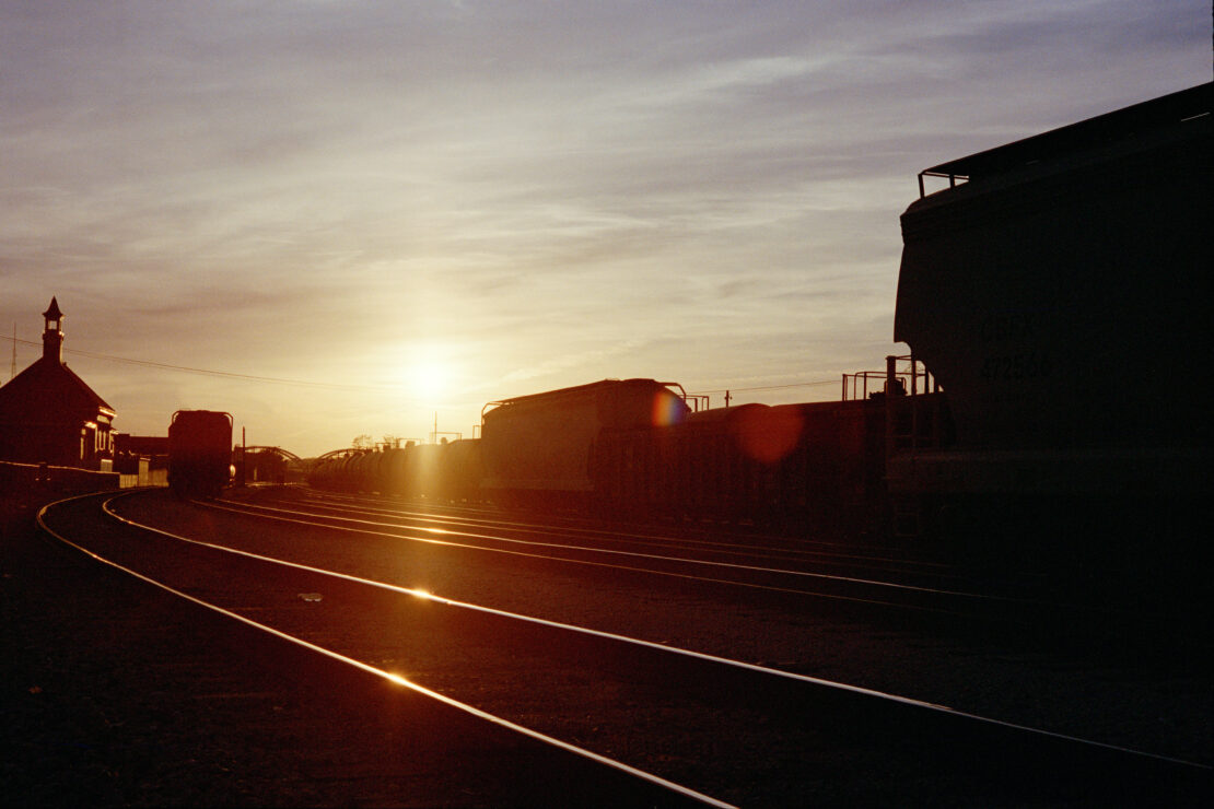 Silhouetted freight trains and curved railway tracks under a golden sunset sky by photographer Olly Burn.
