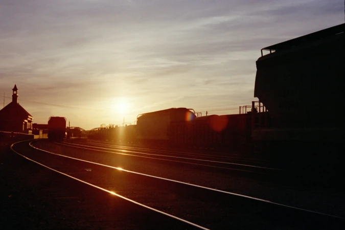 Silhouetted freight trains and curved railway tracks under a golden sunset sky by photographer Olly Burn.