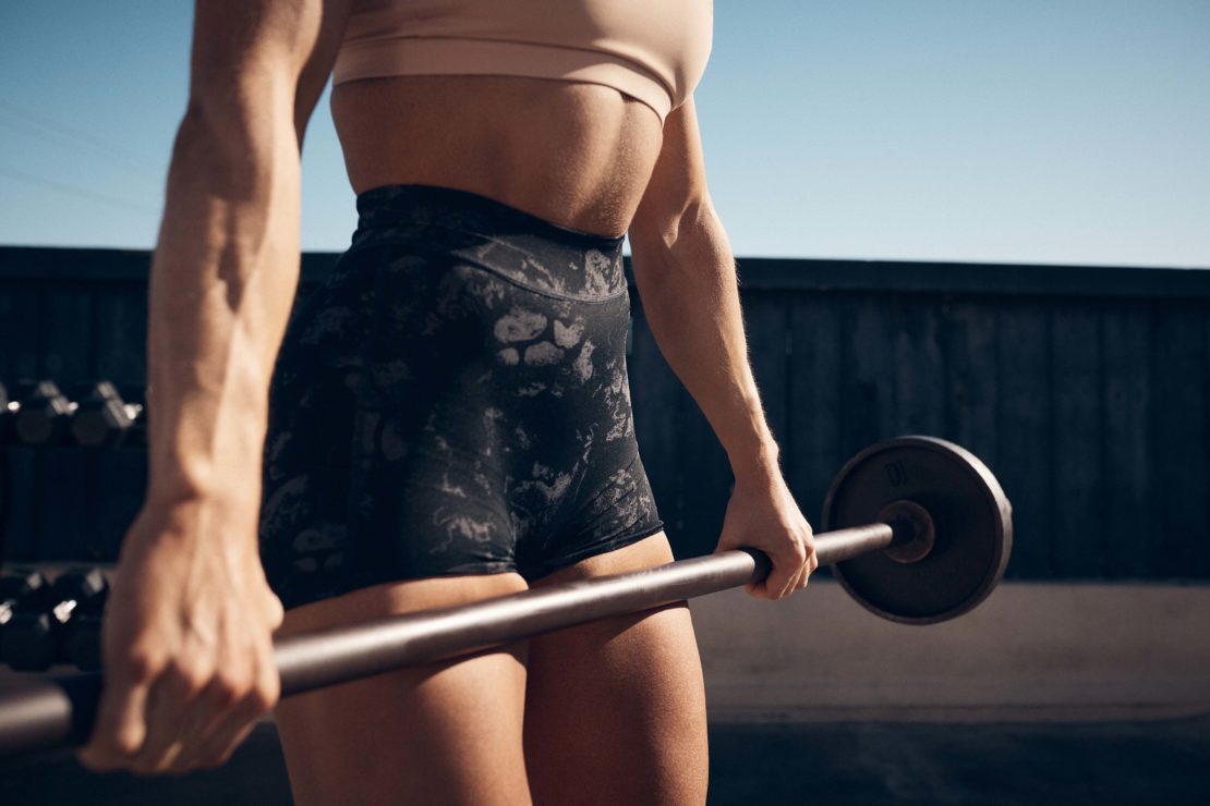 Close-up of fit woman lifting a barbell in an outdoor setting. Focus on arm muscles and form. Fitness, workout, and healthy lifestyle.