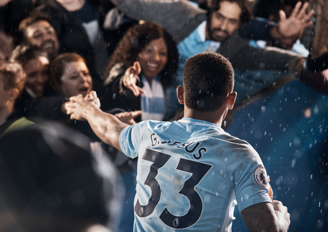 Soccer player in light blue jersey embraces celebrating fans. Joyful sports scene in a stadium with excitement and team spirit.