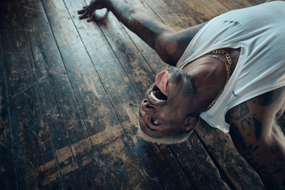 Person with bleached hair lying on their back on a distressed wood floor with their mouth open and tongue sticking out.