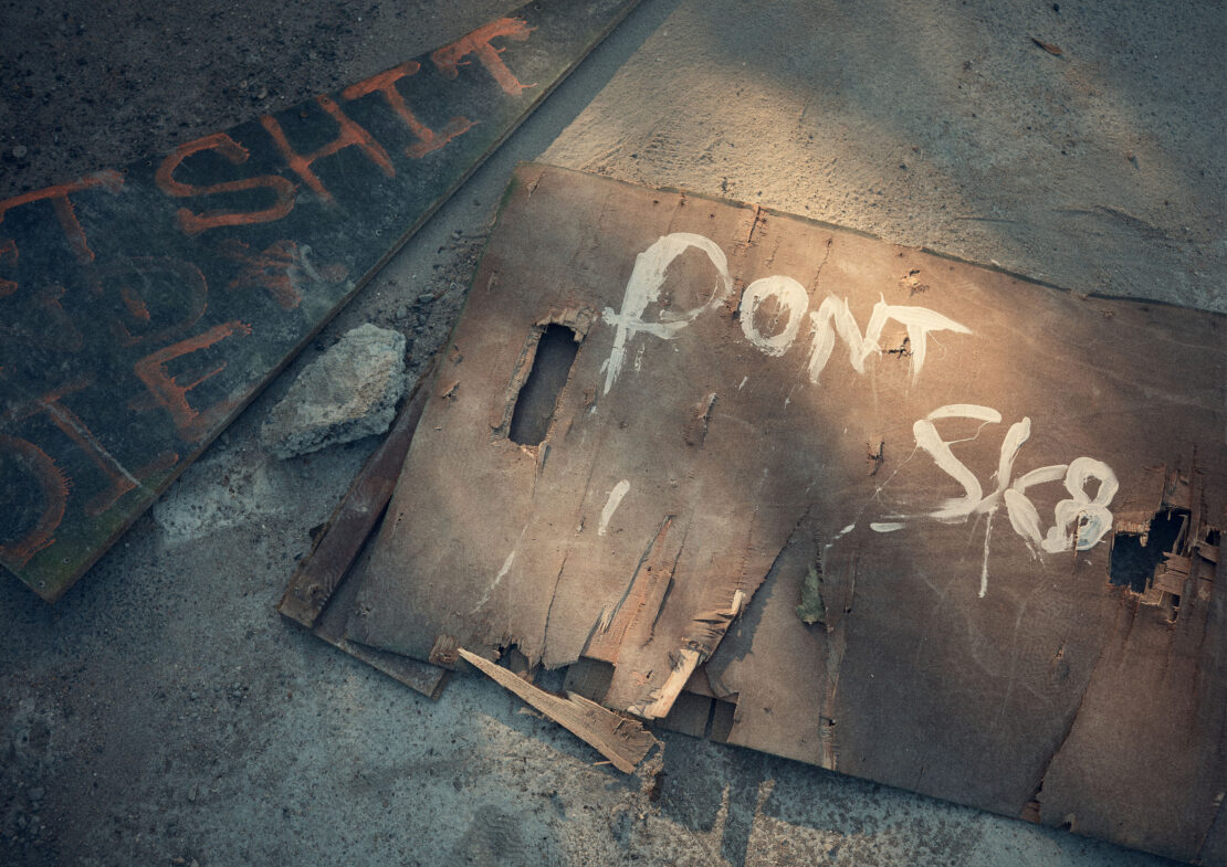 Two weathered wood boards with graffiti lay on concrete, one reading 'DONT SK8' in white paint and another in orange paint.