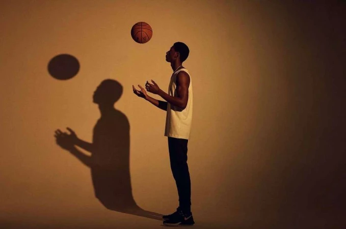 Black man holding a basketball with a dramatic shadow cast against a warm studio wall by photographer Olly Burn.