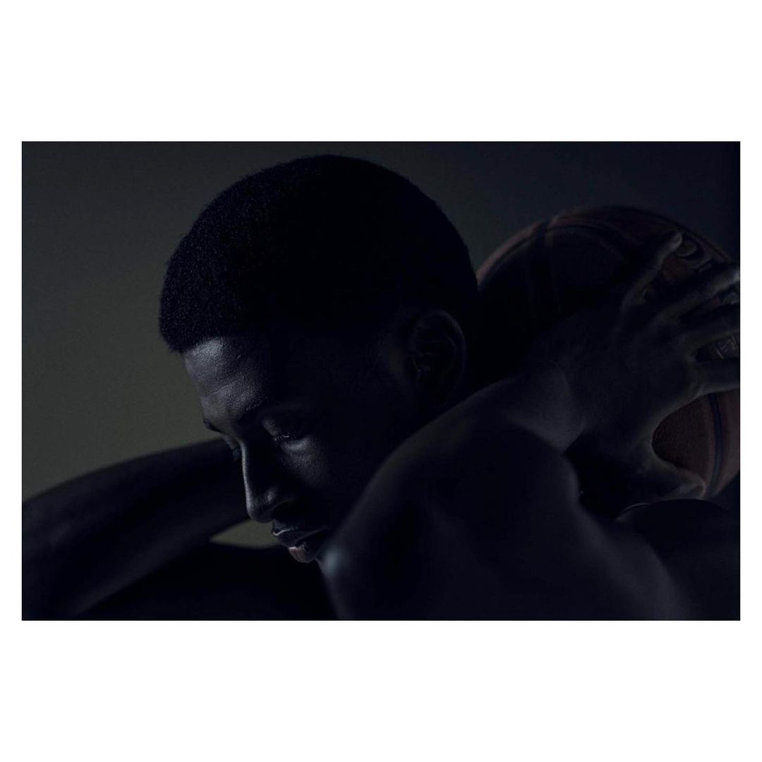 Portrait of a Black man embracing a basketball, showcasing his profile against a dark background with dramatic lighting.