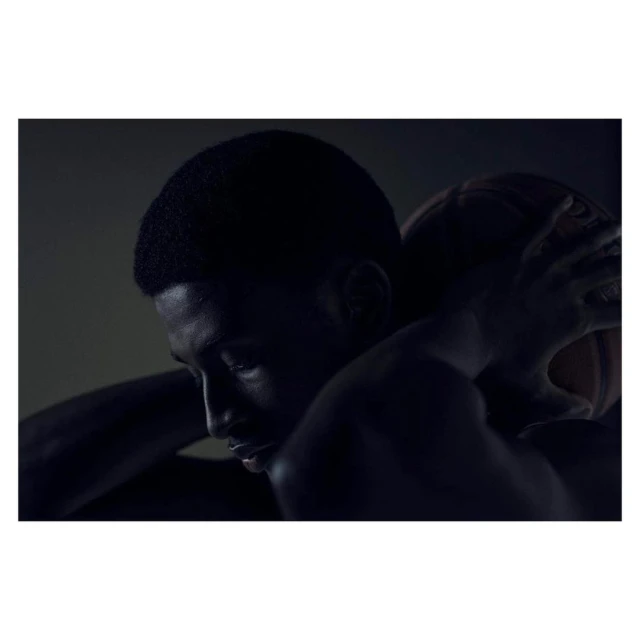 Portrait of a Black man embracing a basketball, showcasing his profile against a dark background with dramatic lighting.
