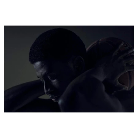 Portrait of a Black man embracing a basketball, showcasing his profile against a dark background with dramatic lighting.